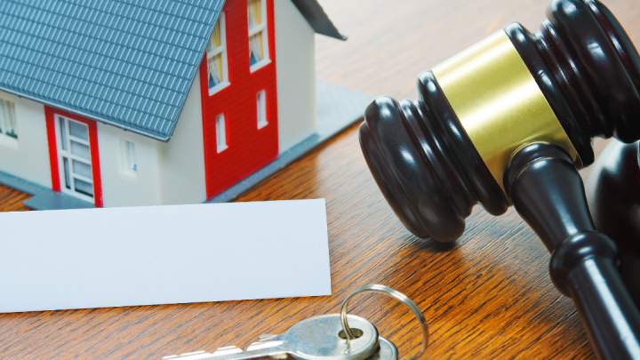 left to right: a small toy house, a deed, two keys, and a gavel sitting on a wooden surface