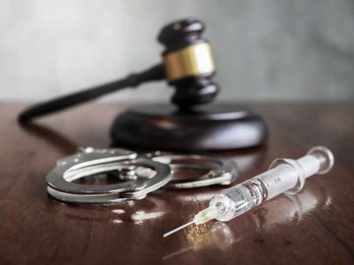 A gavel, a pair of handcuffs, and a syringe sitting on a desk.