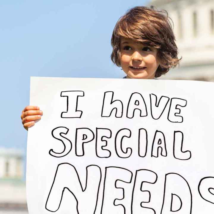 Little boy in front of the Capitol building holding a sign that says "I have special needs."